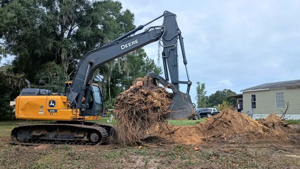 John Deere 200G excavator lifting a whole stump and root ball out of the ground on an Ocala, Florida lot